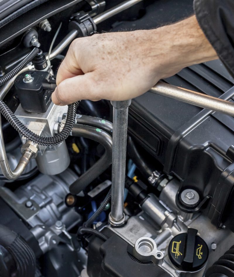 Two hands operating a wrench to remove or tighten a bolt in a latest generation automobile engine